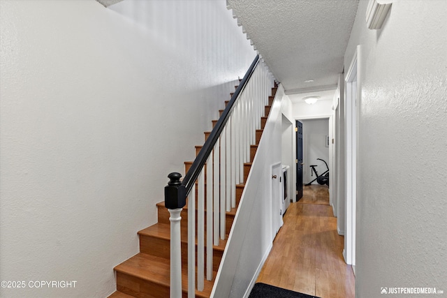 stairs featuring a textured ceiling, a textured wall, and wood finished floors