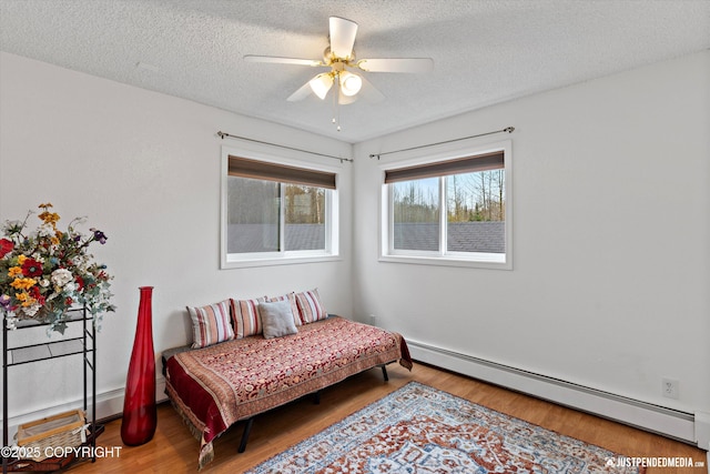 bedroom featuring wood finished floors, baseboards, baseboard heating, a textured ceiling, and a ceiling fan