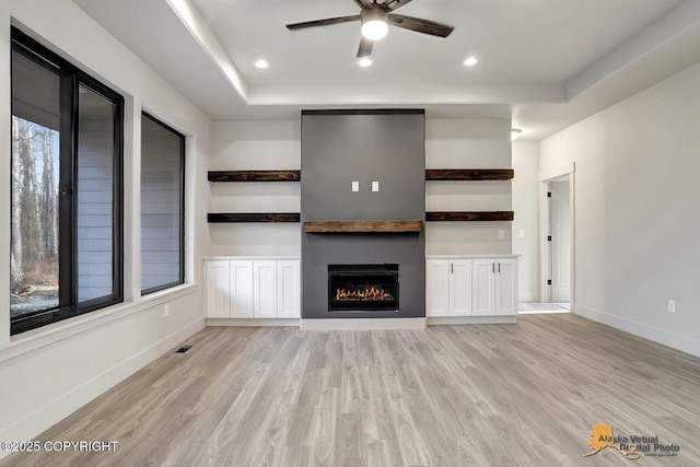 unfurnished living room with light wood-style floors, a large fireplace, baseboards, and a raised ceiling