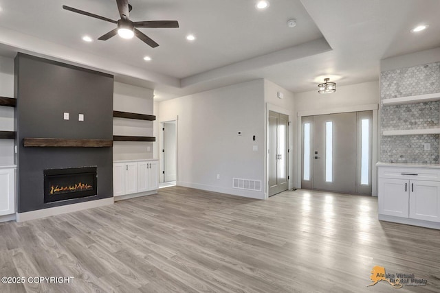 unfurnished living room with light wood-type flooring, visible vents, a glass covered fireplace, and recessed lighting