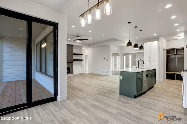 kitchen with light countertops, stainless steel dishwasher, light wood-style floors, a kitchen island with sink, and a sink