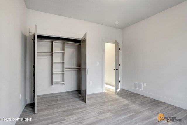 unfurnished bedroom featuring baseboards, a closet, visible vents, and wood finished floors