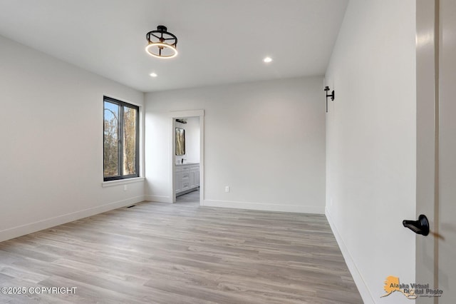 unfurnished bedroom featuring a barn door, recessed lighting, baseboards, light wood finished floors, and ensuite bath