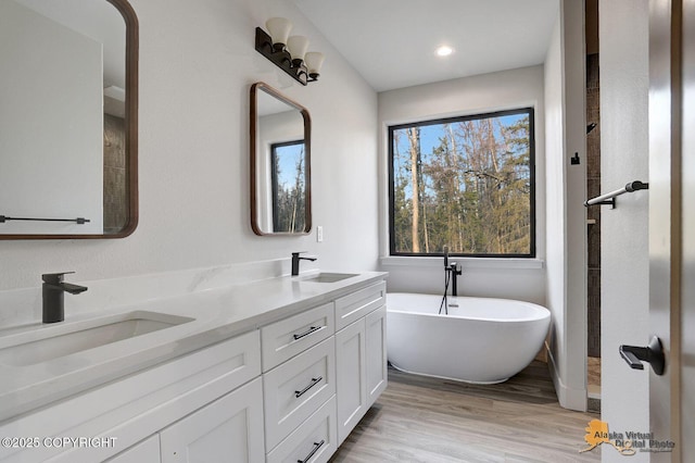 full bathroom with a soaking tub, double vanity, a sink, and wood finished floors