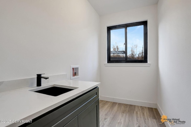 washroom with hookup for a washing machine, a sink, baseboards, light wood-style floors, and cabinet space