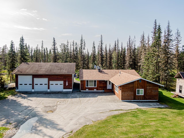 view of front of property with an outbuilding, a forest view, driveway, and a front lawn