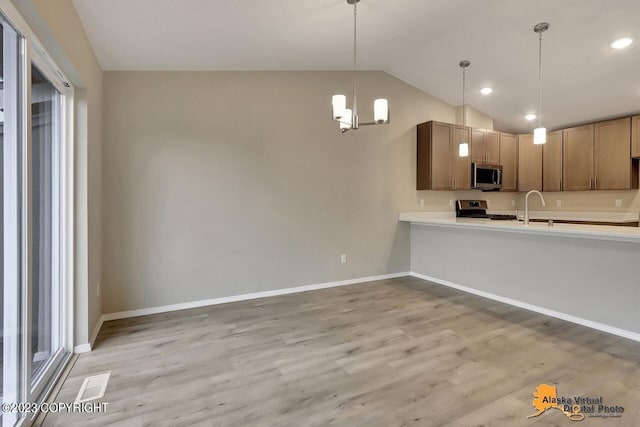 kitchen with pendant lighting, stainless steel appliances, light countertops, light wood-style flooring, and vaulted ceiling