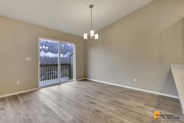 spare room featuring light wood-style flooring, a chandelier, and baseboards