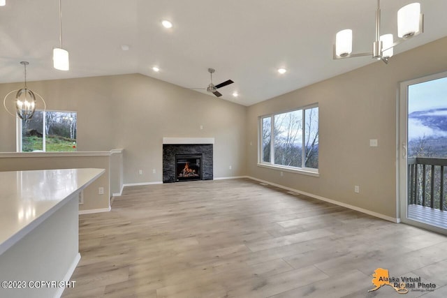 unfurnished living room with lofted ceiling, a stone fireplace, ceiling fan with notable chandelier, and light wood-type flooring