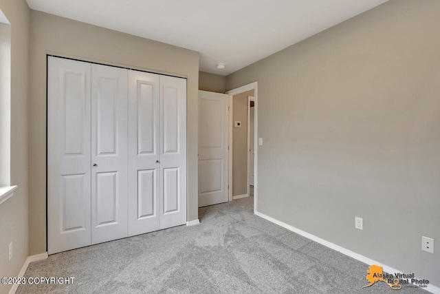 unfurnished bedroom featuring baseboards, a closet, and light colored carpet