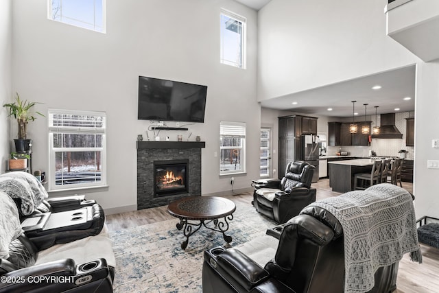 living room with light wood-type flooring, a high ceiling, baseboards, and a stone fireplace