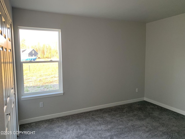 spare room with dark colored carpet and baseboards