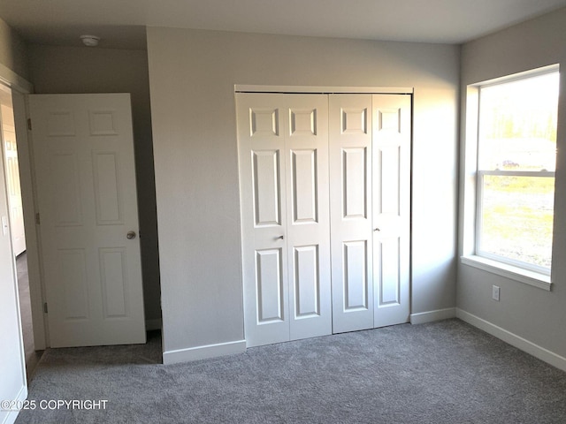 unfurnished bedroom with baseboards, dark colored carpet, and a closet