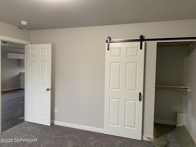 unfurnished bedroom with a barn door, dark carpet, and baseboards