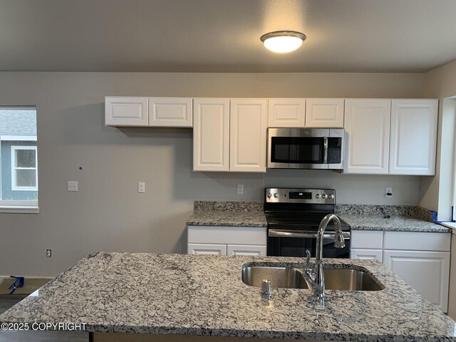 kitchen with light stone counters, appliances with stainless steel finishes, white cabinetry, a sink, and an island with sink