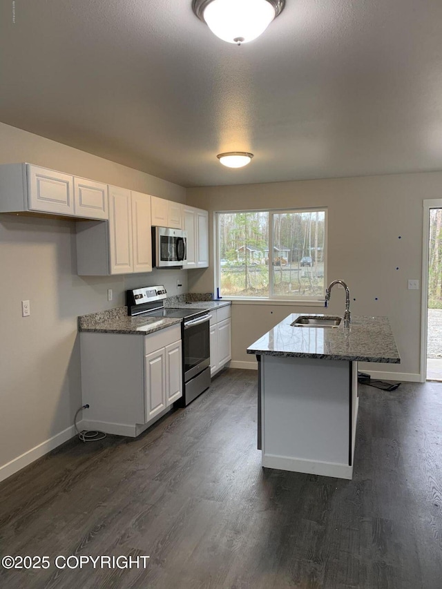 kitchen featuring light stone counters, stainless steel appliances, white cabinets, a sink, and an island with sink