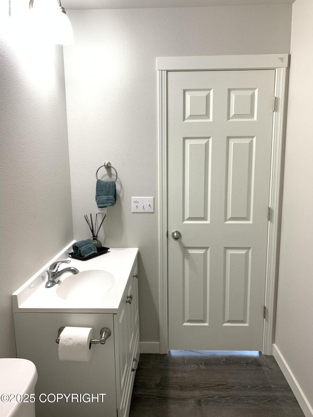 half bath with toilet, baseboards, wood finished floors, and vanity