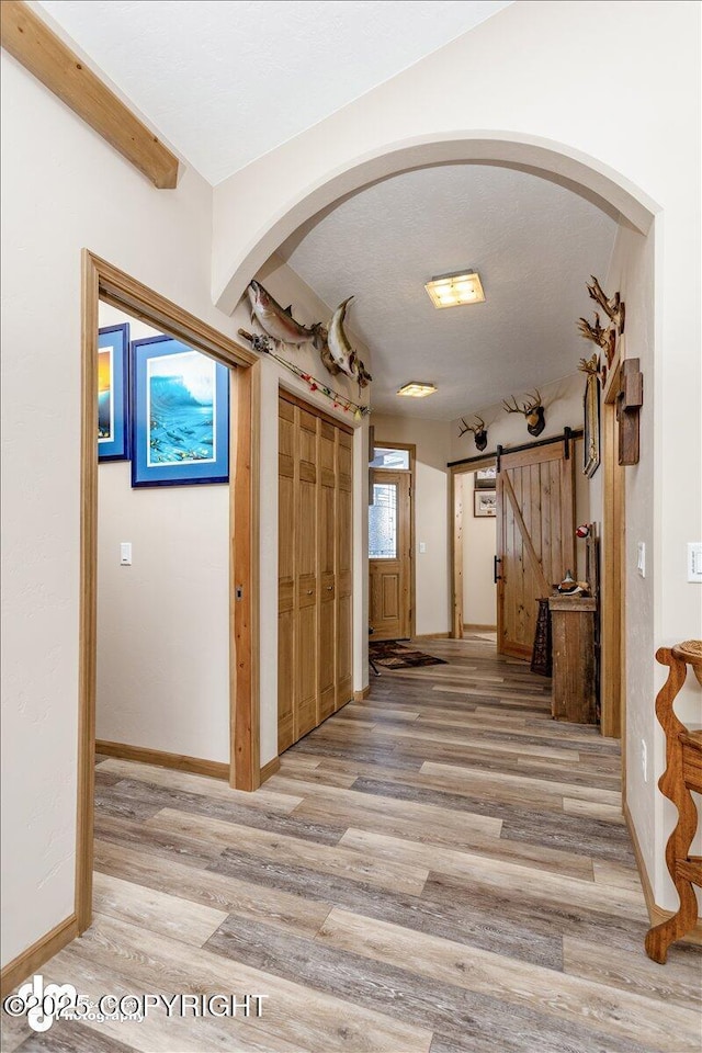 corridor with a barn door, baseboards, arched walkways, wood finished floors, and a textured ceiling