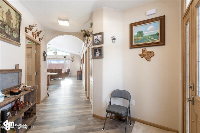 corridor featuring lofted ceiling, baseboards, arched walkways, and wood finished floors