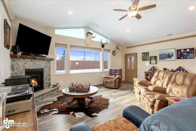 living area featuring light wood-style floors, vaulted ceiling, a stone fireplace, and baseboards