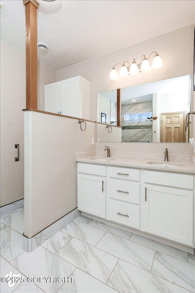 full bathroom featuring marble finish floor, a sink, a textured ceiling, and double vanity