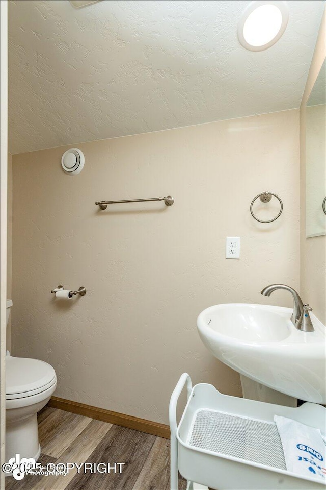 half bathroom featuring toilet, a textured ceiling, baseboards, and wood finished floors