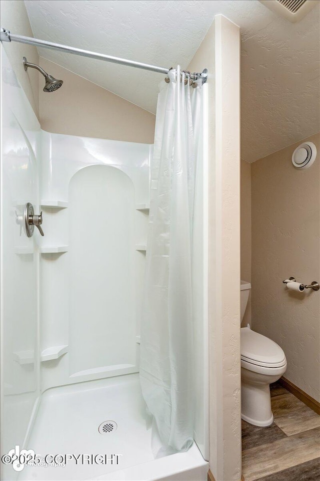 bathroom with a stall shower, lofted ceiling, toilet, wood finished floors, and a textured ceiling