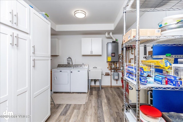 washroom with a sink, water heater, light wood-type flooring, cabinet space, and washing machine and clothes dryer