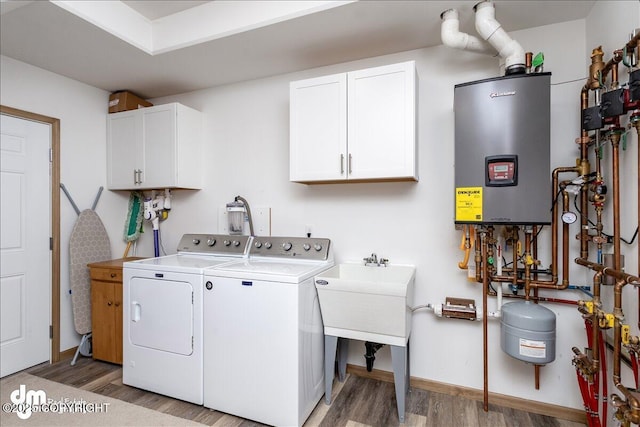 clothes washing area featuring wood finished floors, tankless water heater, cabinet space, and washer and dryer