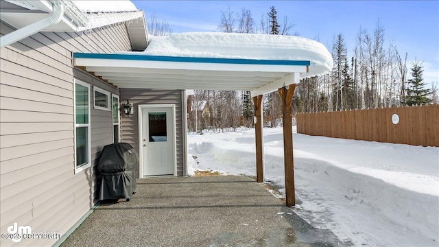 snow covered patio with a carport, fence, and grilling area