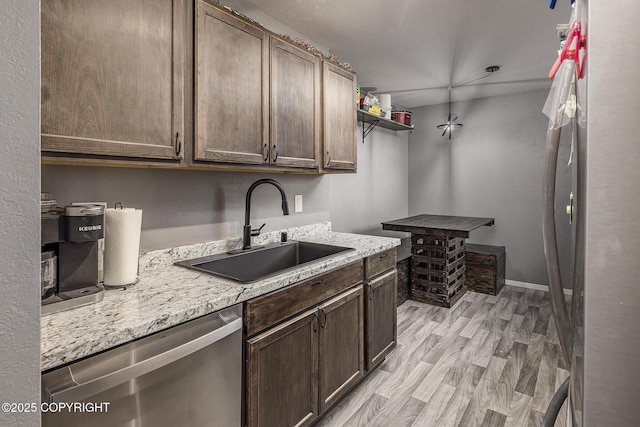 kitchen with light wood finished floors, baseboards, dark brown cabinets, stainless steel dishwasher, and a sink