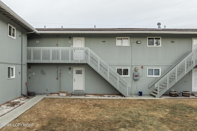 rear view of property with stairway and a lawn