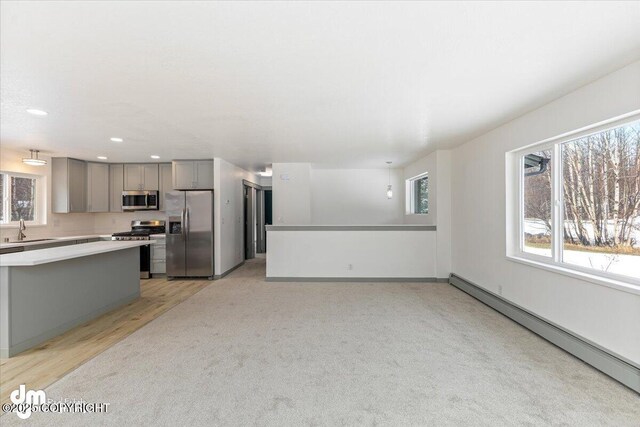 kitchen with stainless steel appliances, gray cabinetry, a baseboard heating unit, a sink, and plenty of natural light