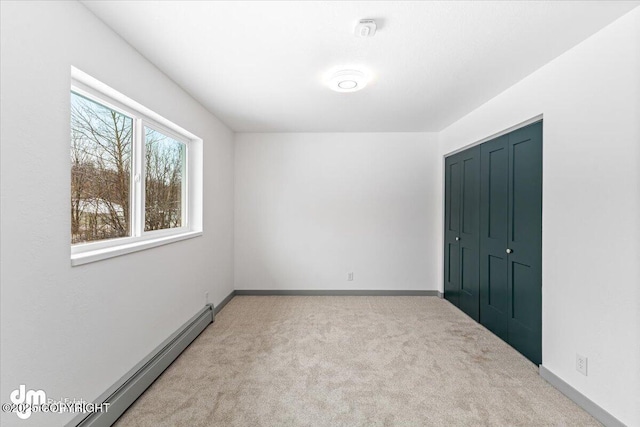 unfurnished bedroom featuring baseboards, a closet, a baseboard heating unit, and carpet flooring