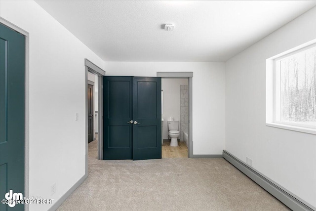 unfurnished bedroom with baseboards, a baseboard radiator, ensuite bathroom, a textured ceiling, and carpet flooring