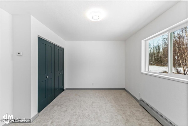 unfurnished bedroom featuring light carpet, a baseboard radiator, baseboards, and a closet