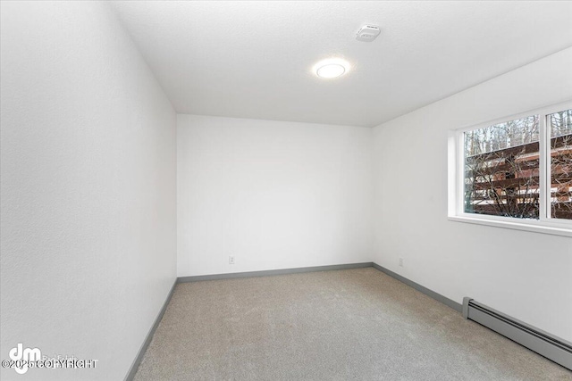 carpeted spare room featuring a baseboard heating unit and baseboards