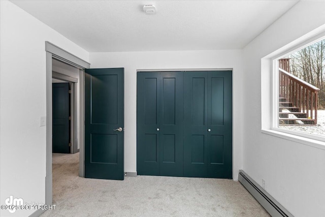 unfurnished bedroom featuring carpet, multiple windows, baseboard heating, and a closet