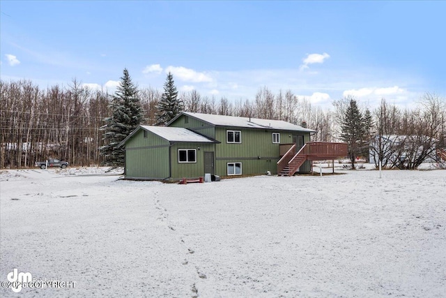 snow covered back of property with a deck and stairway