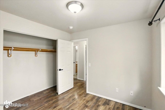 unfurnished bedroom with a closet, dark wood-style flooring, and baseboards
