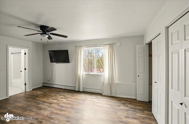 unfurnished bedroom featuring wood finished floors, a baseboard heating unit, and ensuite bath