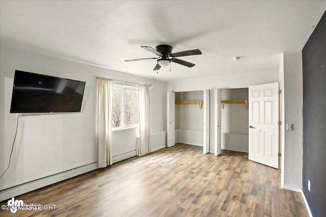 unfurnished bedroom with two closets, a baseboard heating unit, wood finished floors, baseboards, and ceiling fan