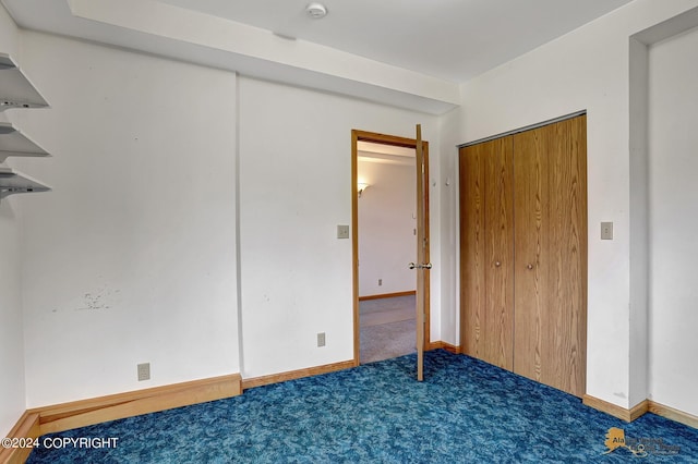 unfurnished bedroom featuring baseboards, dark colored carpet, and a closet