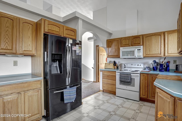 kitchen featuring white appliances, arched walkways, a towering ceiling, light countertops, and light floors