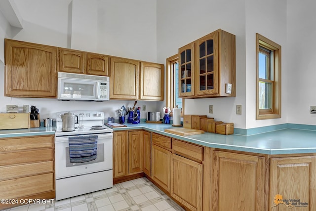 kitchen featuring white appliances, glass insert cabinets, a high ceiling, light countertops, and light floors