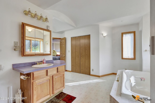 bathroom featuring a healthy amount of sunlight, vanity, baseboards, and a bath