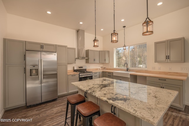 kitchen with light stone counters, stainless steel appliances, gray cabinets, a sink, and wall chimney range hood