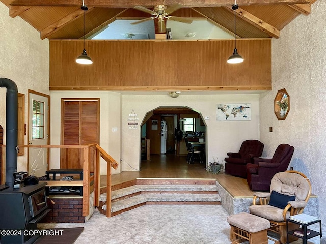 carpeted living area featuring wood ceiling, a wood stove, a textured wall, and beam ceiling