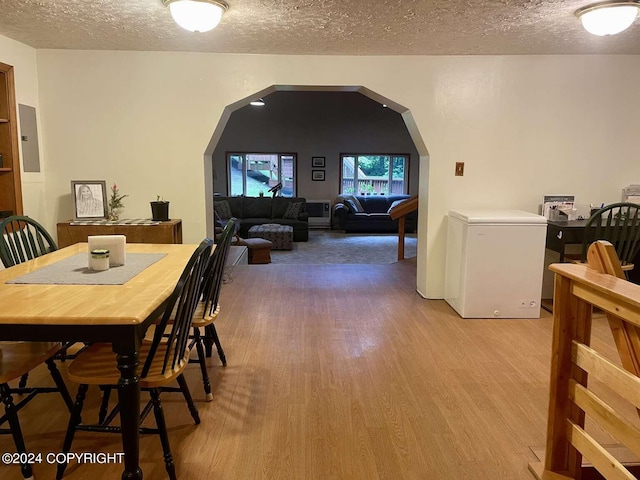 dining space with light wood-type flooring, arched walkways, and a textured ceiling