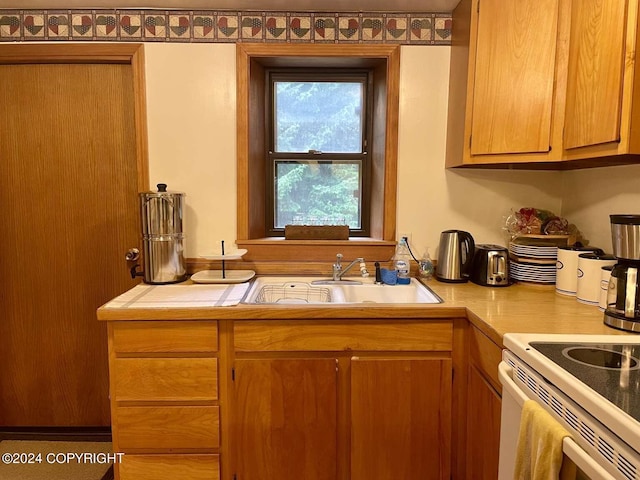 kitchen with brown cabinetry, white range with electric stovetop, light countertops, and a sink